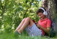 Elementary-aged boy reading a book outside while wearing headphones